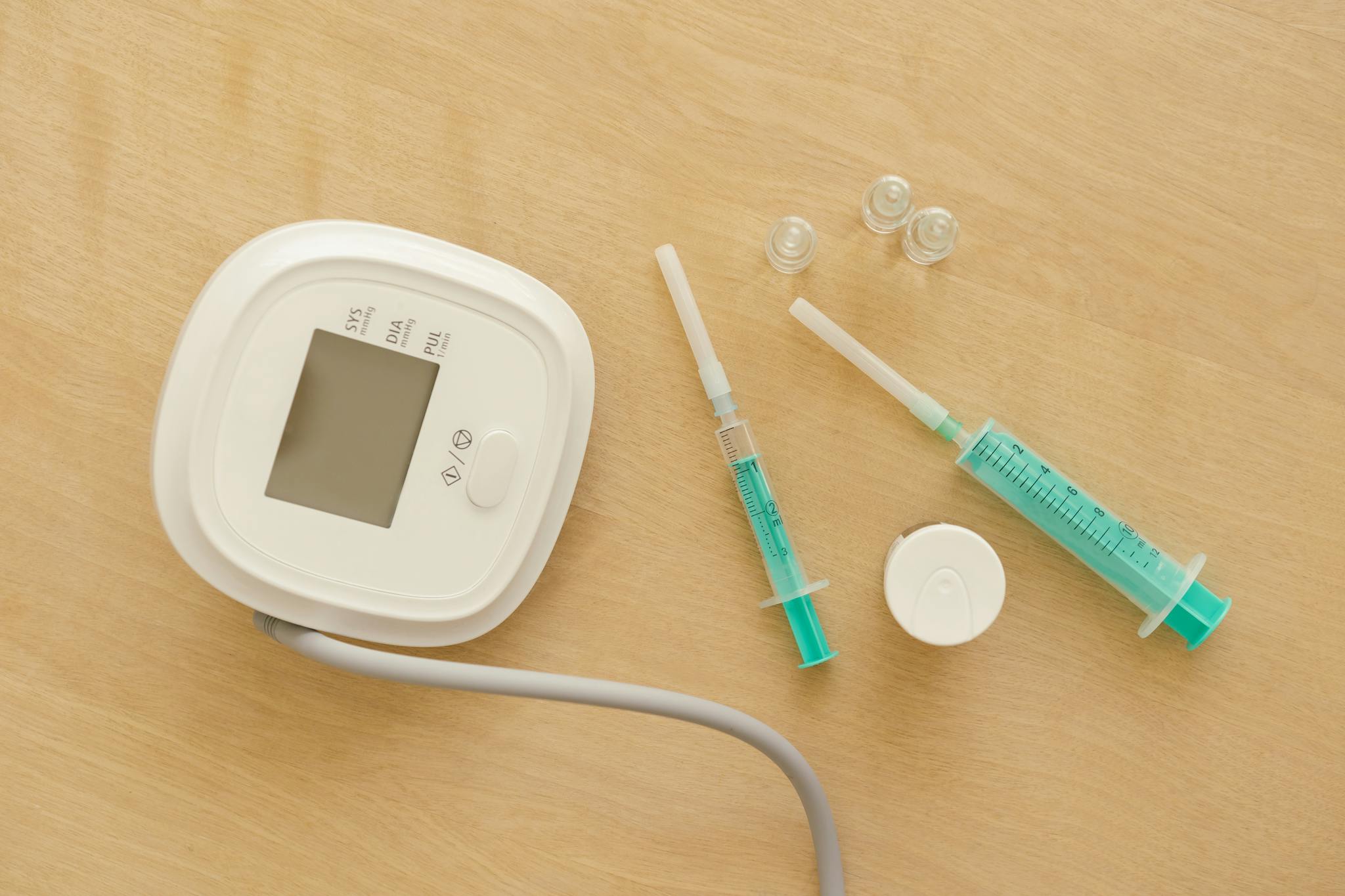 Flat lay of medical equipment including a sphygmomanometer and syringes on a wooden surface.